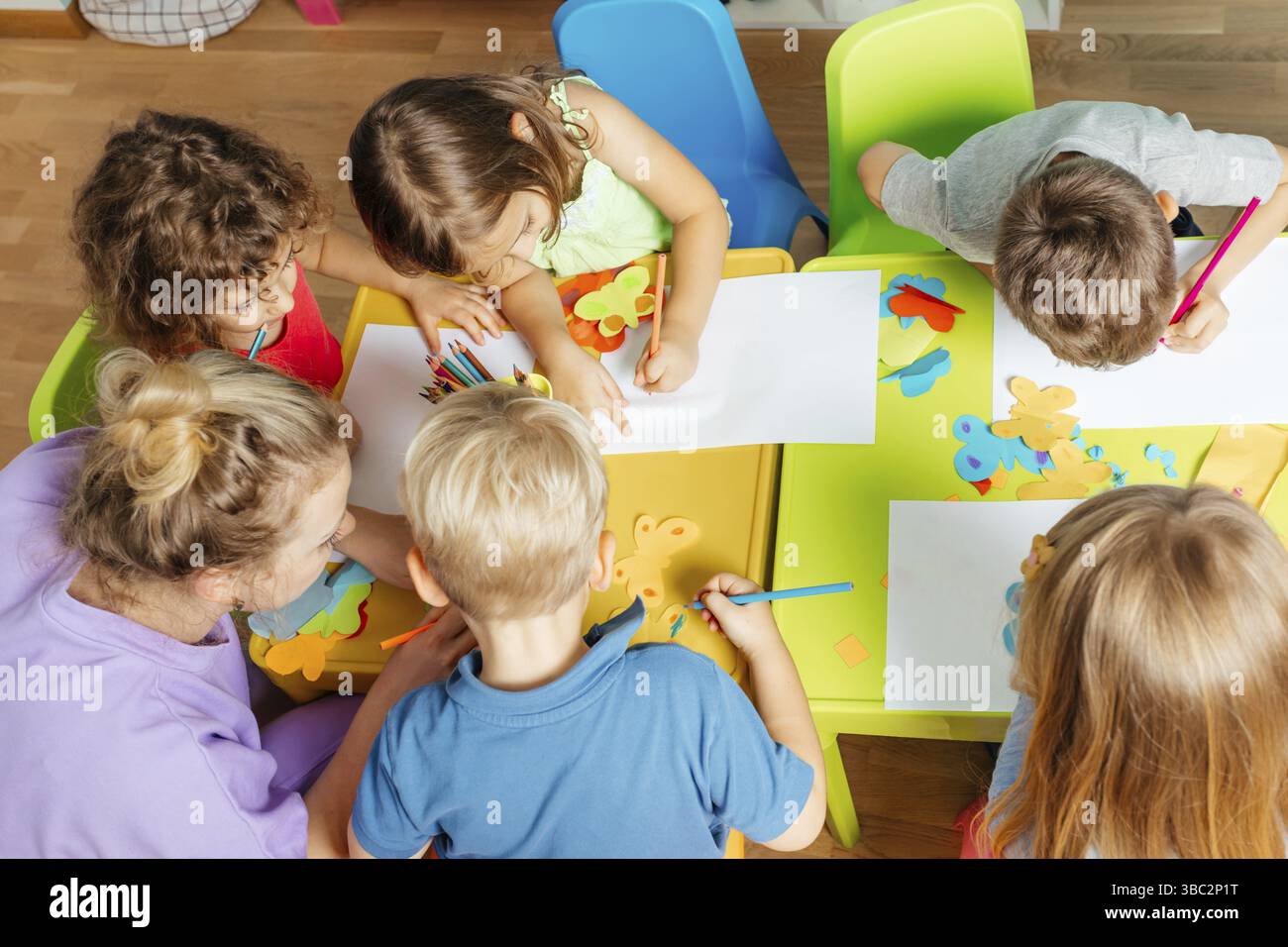 Cours d'art au jardin d'enfants, vue de dessus. Beaux enfants collant et coupant du papier sur des tables en plastique coloré. Concept de développement de l'enfant Banque D'Images