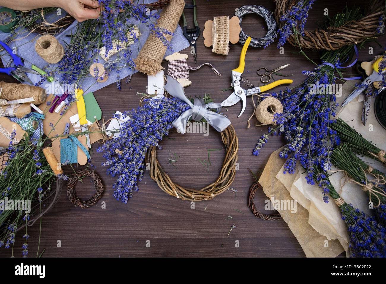 Vue de dessus couronne faite à la main décorée de fleurs de lavande sur une surface en bois. Variété de matériaux et d'outils pour fleurs faites à la main. Bouquet d'aromati frais Banque D'Images