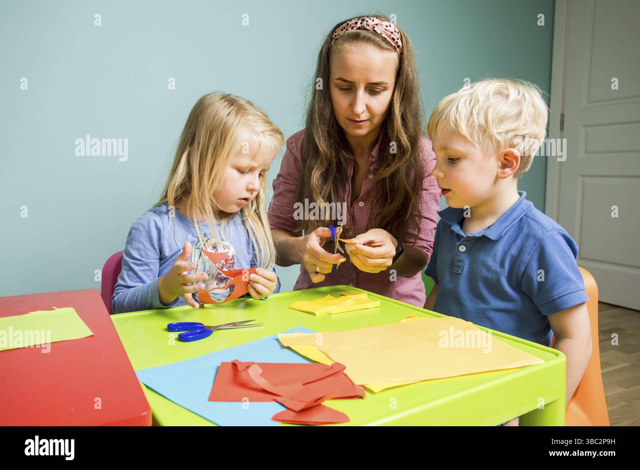 Les enfants d'âge préscolaire découpent différentes figures du papier coloré avec l'enseignant. Le concept de développement de la pensée créative dans les pres Banque D'Images