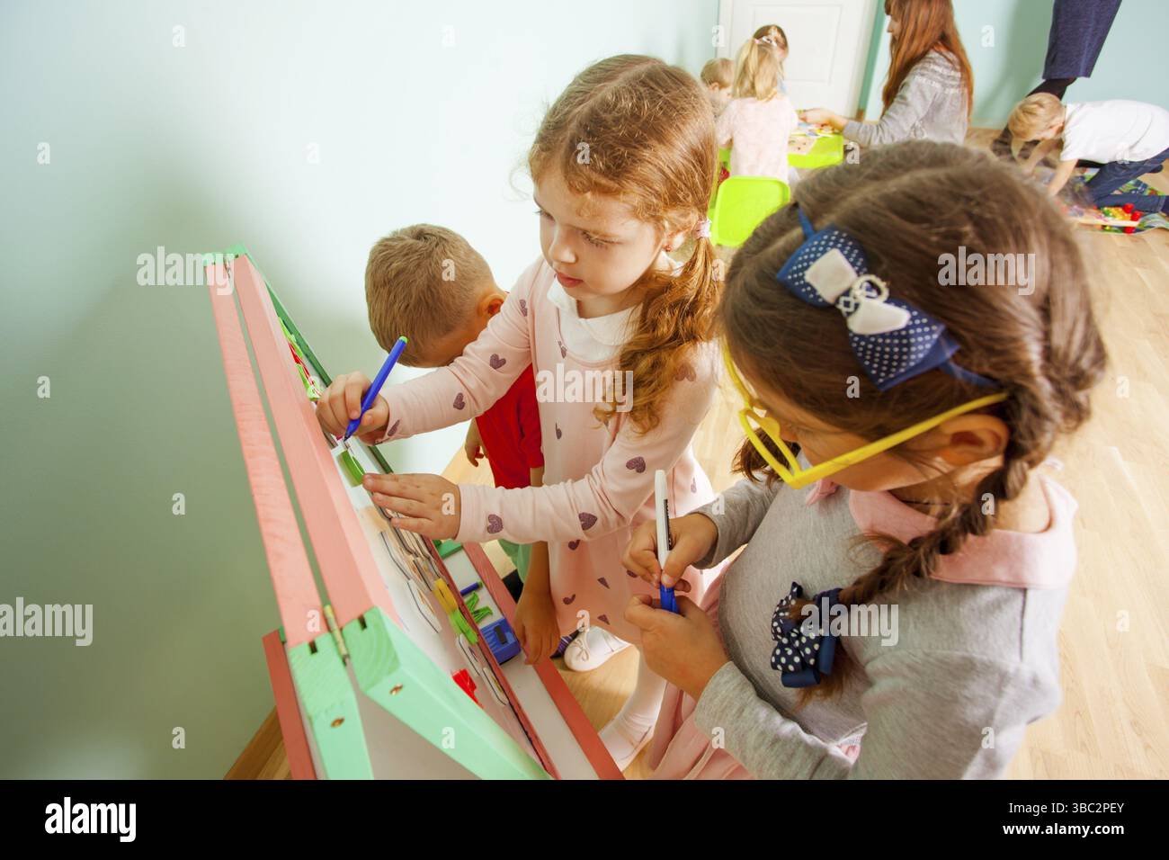 Les enfants de divers âges résolvent les problèmes mathématiques sur le tableau de la magnétie. Fille joue le professeur à la garderie Banque D'Images