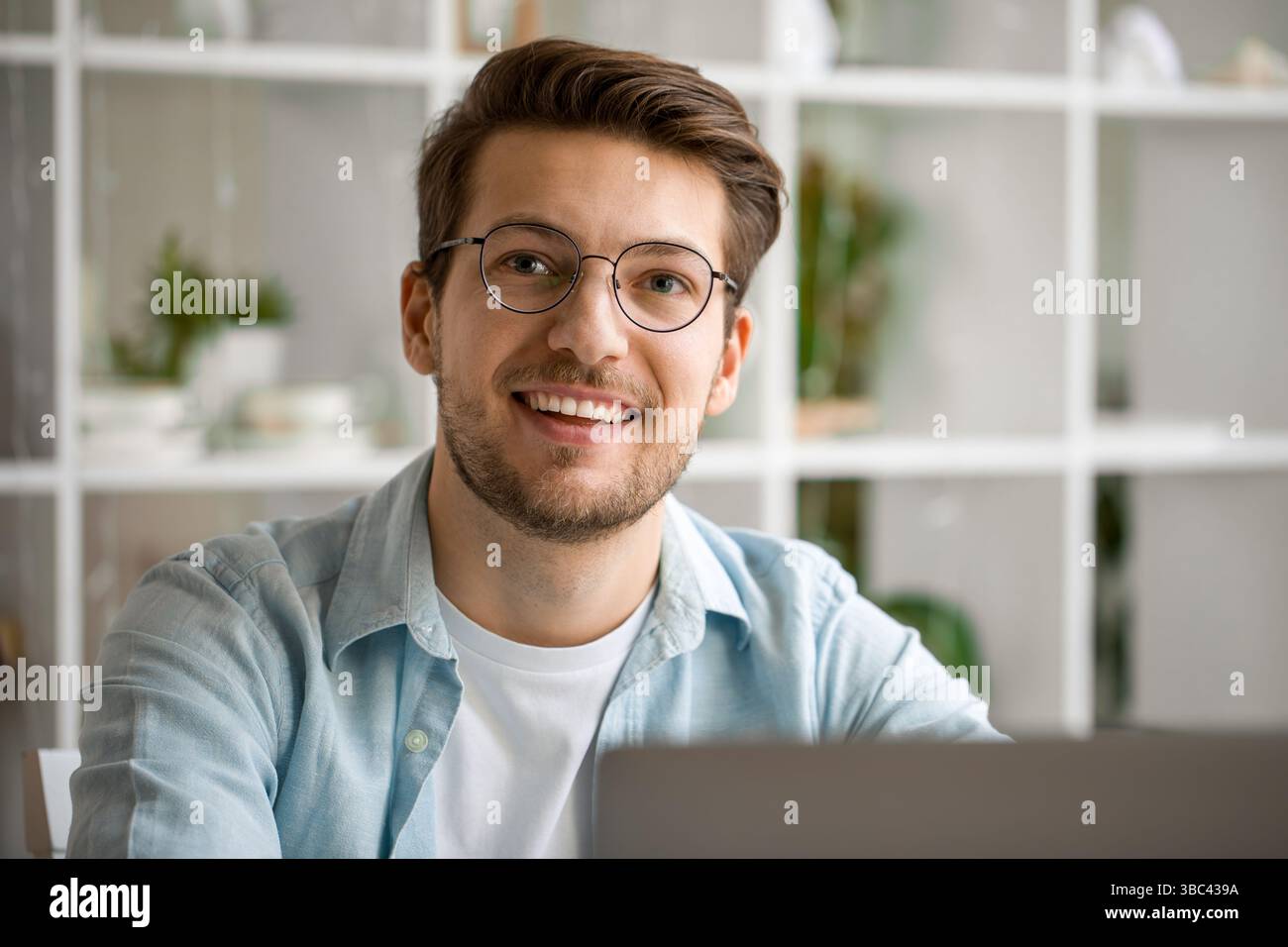 Portrait d'un jeune homme confiant dans des lunettes souriant à la caméra tout en travaillant à distance de la maison Banque D'Images