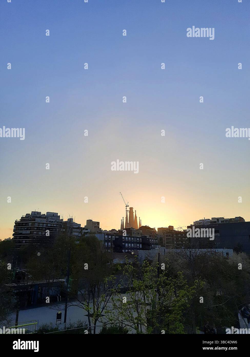 La célèbre basilique de la Sagrada Familia vue de loin en silhouette à l'heure dorée avec une lumière douce sur les bâtiments de la ville et la végétation Banque D'Images