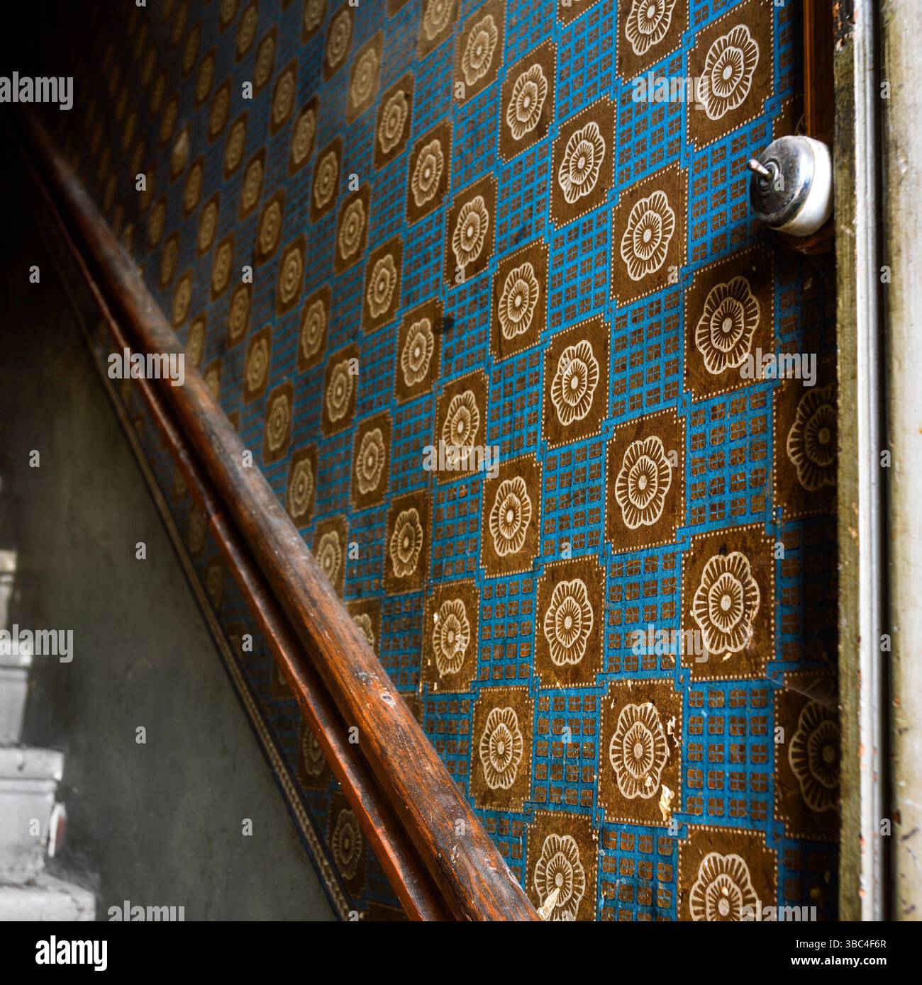 Une vue rapprochée d'un vieux papier peint tapissant les murs d'un couloir d'escalier, avec un motif géométrique avec des motifs floraux et une main courante en bois Banque D'Images