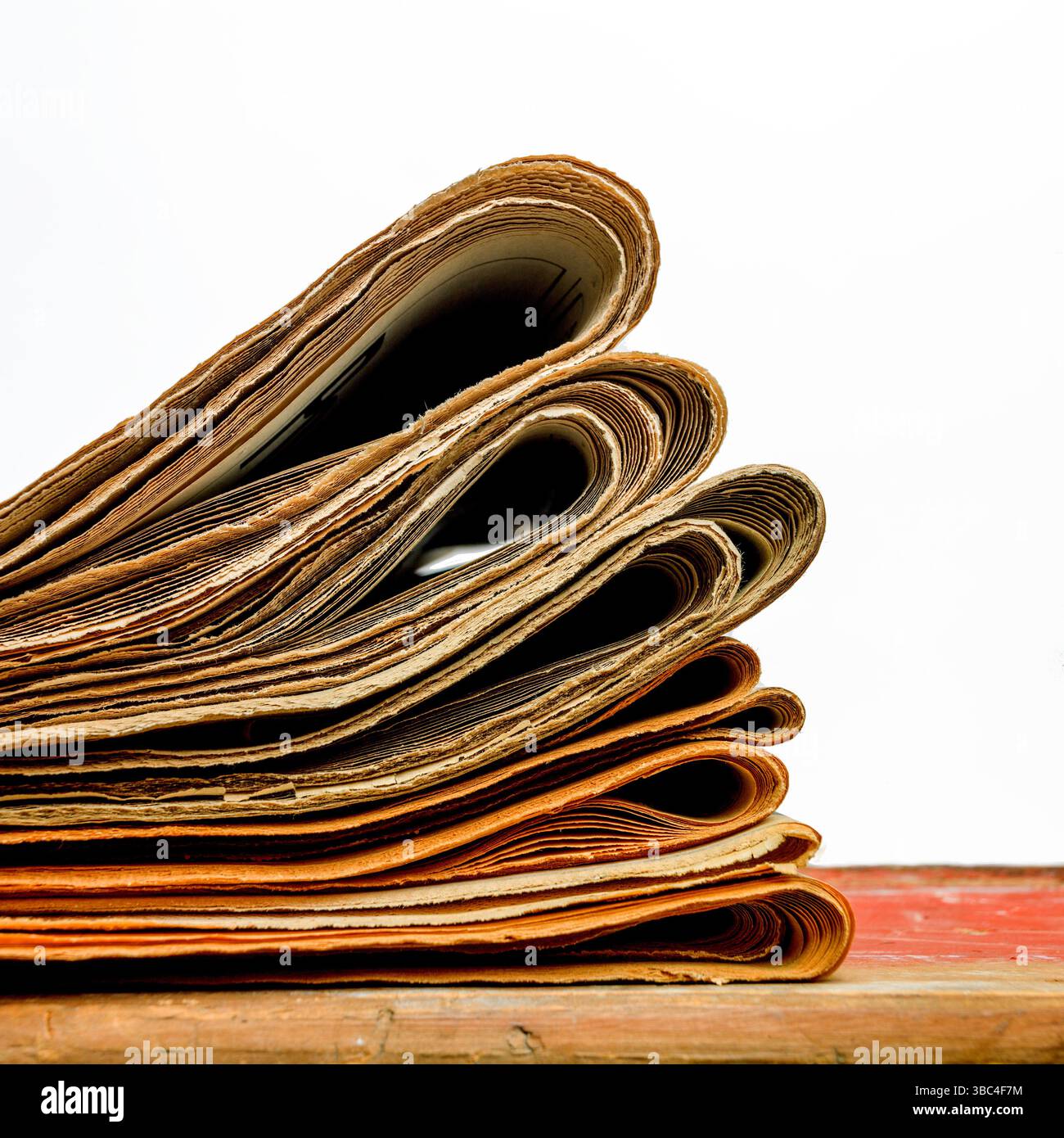 Une pile de journaux repose soigneusement sur un fond blanc, affichant un assortiment de pages pliées avec des articles imprimés et des images. Banque D'Images