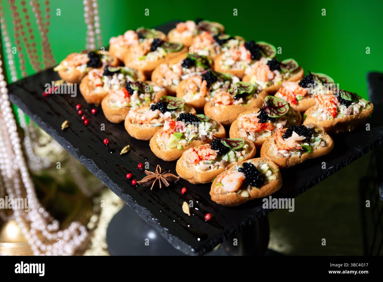 Canapés de fruits de mer élégants garnis de crevettes, de caviar, d'herbes et d'un mélange de salade, magnifiquement disposés sur un plateau de service sombre. Banque D'Images