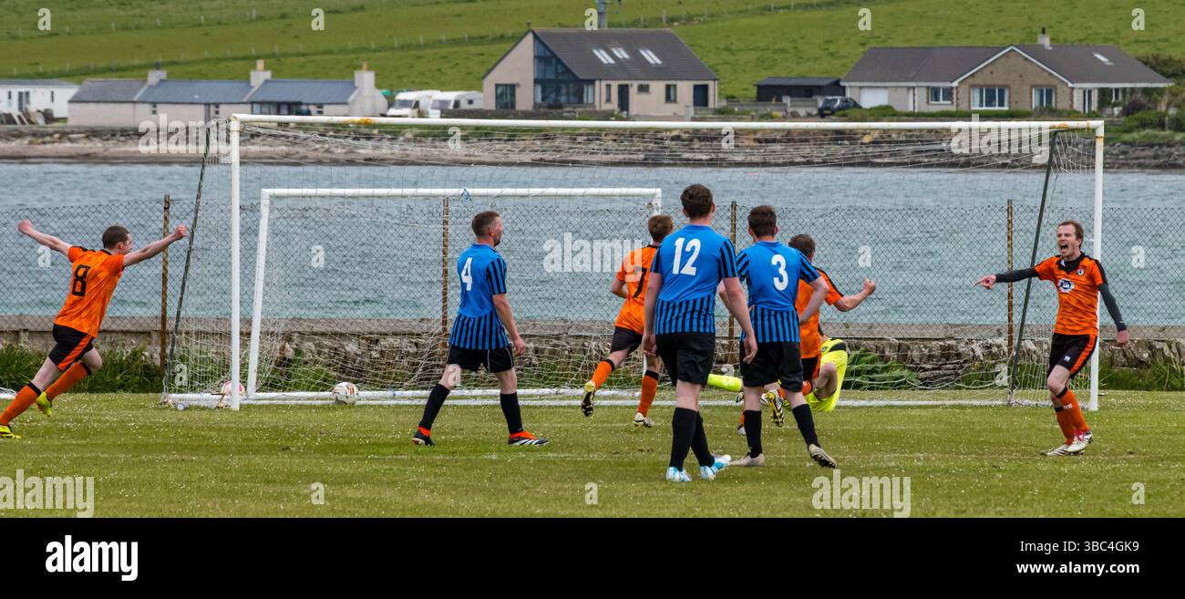 Pierowall, Westray, Orcades, Écosse, Royaume-Uni. Papa Westray v Sanday 2ème match de football matc dans la ligue Orkney amateur Football Association ou Coupe Orcadienne : la famille Houston trigénérationnelle) dans l'équipe de Papa Westray (alias les Doondies en maillots orange) allant dans l'âge de 63 à 19 ans, avec une population de 90 et aucun terrain de football à pratiquer sur perdre 7-1 ayant perdu 6-0 dans la 1ère manche le 6 mai. Ils étaient ravis de marquer un but avec un penalty dans les dernières minutes du match. De nombreux habitants de Papa Westray sont venus de l'île pour les soutenir. Pic : le but de Papay Banque D'Images