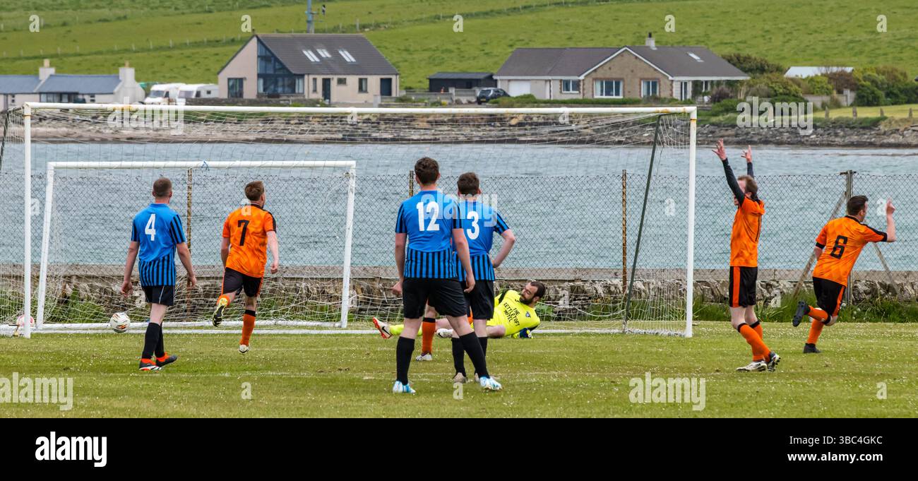 Pierowall, Westray, Orcades, Écosse, Royaume-Uni. Papa Westray v Sanday 2ème match de football matc dans la ligue Orkney amateur Football Association ou Coupe Orcadienne : la famille Houston trigénérationnelle) dans l'équipe de Papa Westray (alias les Doondies en maillots orange) allant dans l'âge de 63 à 19 ans, avec une population de 90 et aucun terrain de football à pratiquer sur perdre 7-1 ayant perdu 6-0 dans la 1ère manche le 6 mai. Ils étaient ravis de marquer un but avec un penalty dans les dernières minutes du match. De nombreux habitants de Papa Westray sont venus de l'île pour les soutenir. Pic : le but de Papay Banque D'Images