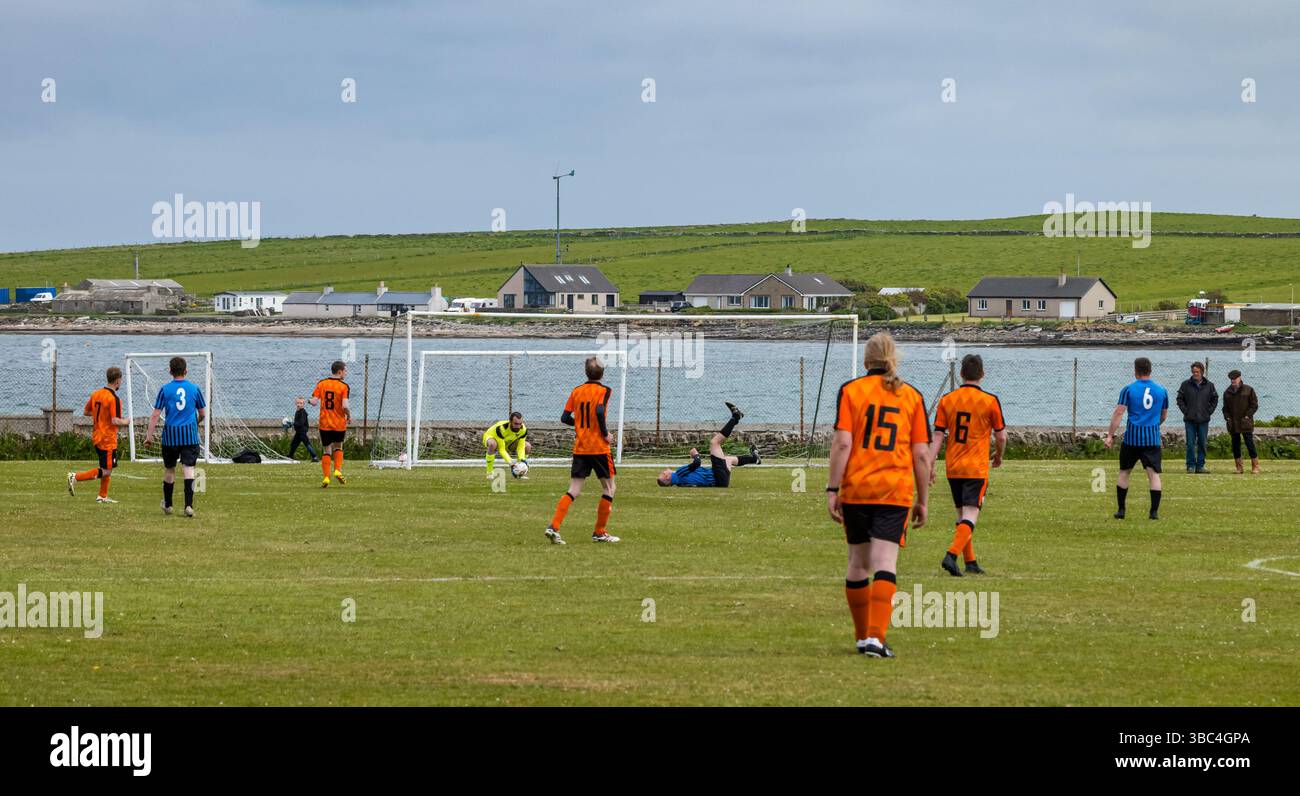 Pierowall, Westray, Orcades, Écosse, Royaume-Uni. Papa Westray v Sanday 2nd leg football matc in Orkney amateur Football Association League ou Orcadian Cup : la famille Houston trigénérationnelle) dans l'équipe de Papa Westray (alias les Doondies en maillots orange) allant dans l'âge de 63 à 19 ans, avec une population de 90 et aucun terrain de football à pratiquer sur perdre 7-1 ayant perdu 6-0 dans la 1ère manche. Ils étaient ravis de marquer un but avec un penalty dans les dernières minutes du match. De nombreux habitants de Papa Westray sont venus de l'île pour les soutenir. Crédit : Sally Anderson/Alamy Live News Banque D'Images