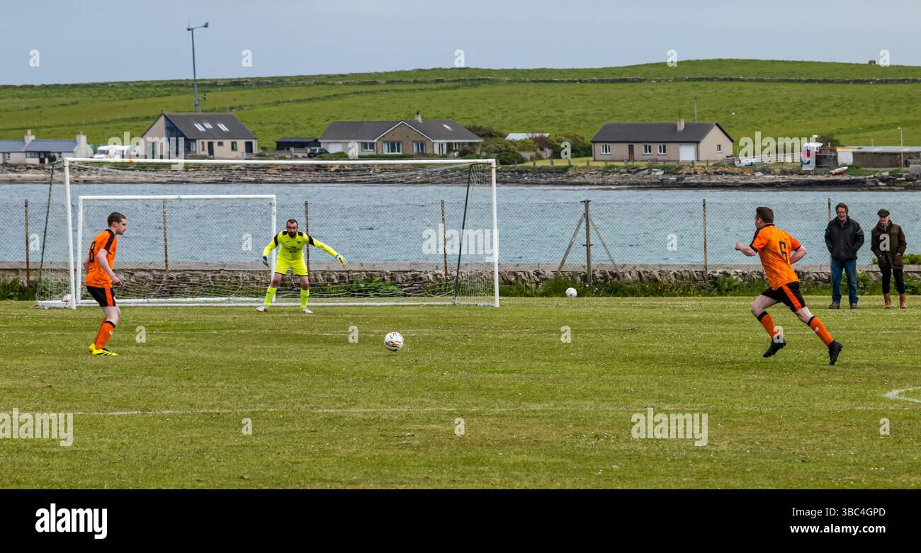 Pierowall, Westray, Orcades, Écosse, Royaume-Uni. Papa Westray v Sanday 2nd leg football matc in Orkney amateur Football Association League ou Orcadian Cup : la famille Houston trigénérationnelle) dans l'équipe de Papa Westray (alias les Doondies en maillots orange) allant dans l'âge de 63 à 19 ans, avec une population de 90 et aucun terrain de football à pratiquer sur perdre 7-1 ayant perdu 6-0 dans la 1ère manche. Ils étaient ravis de marquer un but avec un penalty dans les dernières minutes du match. De nombreux habitants de Papa Westray sont venus de l'île pour les soutenir. Crédit : Sally Anderson/Alamy Live News Banque D'Images
