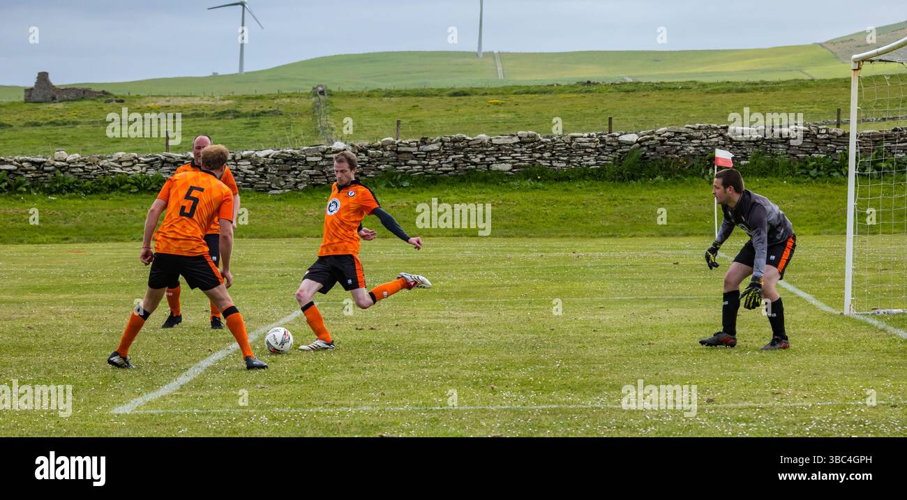 Pierowall, Westray, Orcades, Écosse, Royaume-Uni. Papa Westray v Sanday 2nd leg football matc in Orkney amateur Football Association League ou Orcadian Cup : la famille Houston trigénérationnelle) dans l'équipe de Papa Westray (alias les Doondies en maillots orange) allant dans l'âge de 63 à 19 ans, avec une population de 90 et aucun terrain de football à pratiquer sur perdre 7-1 ayant perdu 6-0 dans la 1ère manche. Ils étaient ravis de marquer un but avec un penalty dans les dernières minutes du match. De nombreux habitants de Papa Westray sont venus de l'île pour les soutenir. Crédit : Sally Anderson/Alamy Live News Banque D'Images