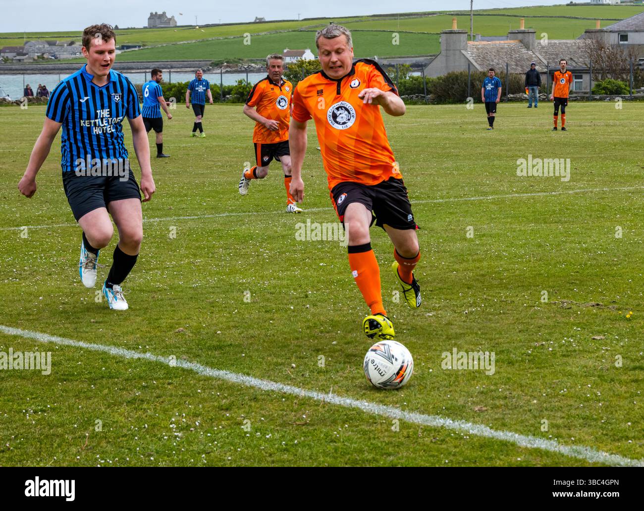 Pierowall, Westray, Orcades, Écosse, Royaume-Uni. Papa Westray v Sanday 2nd leg football matc in Orkney amateur Football Association League ou Orcadian Cup : la famille Houston trigénérationnelle) dans l'équipe de Papa Westray (alias les Doondies en maillots orange) allant dans l'âge de 63 à 19 ans, avec une population de 90 et aucun terrain de football à pratiquer sur perdre 7-1 ayant perdu 6-0 dans la 1ère manche. Ils étaient ravis de marquer un but avec un penalty dans les dernières minutes du match. De nombreux habitants de Papa Westray sont venus de l'île pour les soutenir. Crédit : Sally Anderson/Alamy Live News Banque D'Images