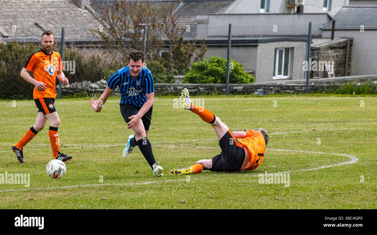 Pierowall, Westray, Orcades, Écosse, Royaume-Uni. Papa Westray v Sanday 2nd leg football matc in Orkney amateur Football Association League ou Orcadian Cup : la famille Houston trigénérationnelle) dans l'équipe de Papa Westray (alias les Doondies en maillots orange) allant dans l'âge de 63 à 19 ans, avec une population de 90 et aucun terrain de football à pratiquer sur perdre 7-1 ayant perdu 6-0 dans la 1ère manche. Ils étaient ravis de marquer un but avec un penalty dans les dernières minutes du match. De nombreux habitants de Papa Westray sont venus de l'île pour les soutenir. Crédit : Sally Anderson/Alamy Live News Banque D'Images