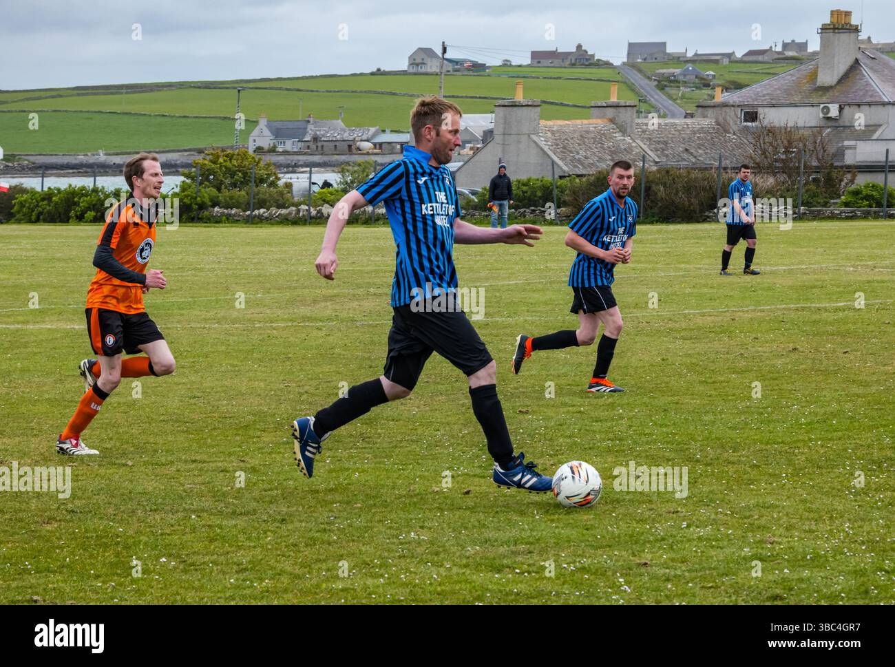 Pierowall, Westray, Orcades, Écosse, Royaume-Uni. Papa Westray v Sanday 2nd leg football matc in Orkney amateur Football Association League ou Orcadian Cup : la famille Houston trigénérationnelle) dans l'équipe de Papa Westray (alias les Doondies en maillots orange) allant dans l'âge de 63 à 19 ans, avec une population de 90 et aucun terrain de football à pratiquer sur perdre 7-1 ayant perdu 6-0 dans la 1ère manche. Ils étaient ravis de marquer un but avec un penalty dans les dernières minutes du match. De nombreux habitants de Papa Westray sont venus de l'île pour les soutenir. Crédit : Sally Anderson/Alamy Live News Banque D'Images