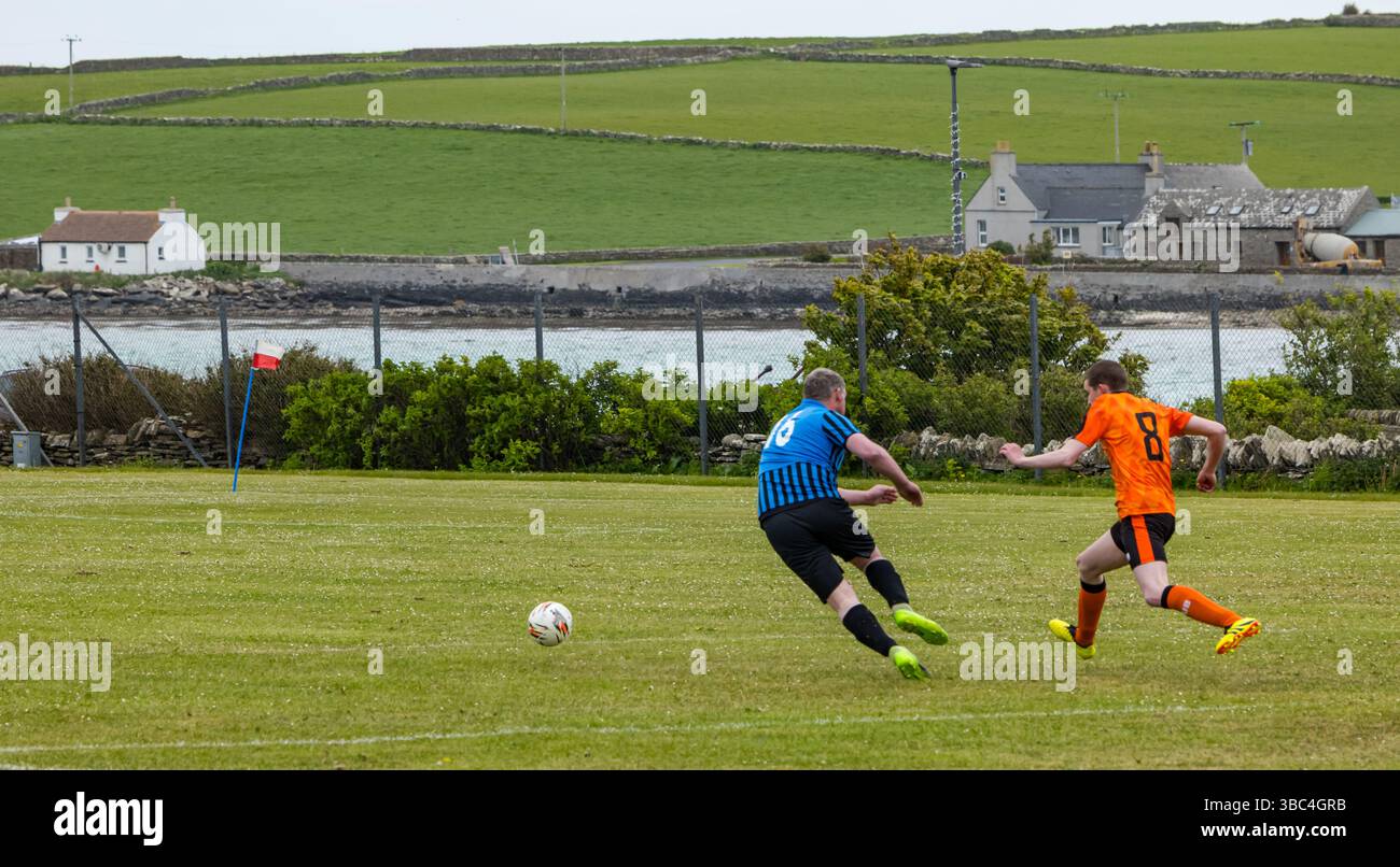 Pierowall, Westray, Orcades, Écosse, Royaume-Uni. Papa Westray v Sanday 2nd leg football matc in Orkney amateur Football Association League ou Orcadian Cup : la famille Houston trigénérationnelle) dans l'équipe de Papa Westray (alias les Doondies en maillots orange) allant dans l'âge de 63 à 19 ans, avec une population de 90 et aucun terrain de football à pratiquer sur perdre 7-1 ayant perdu 6-0 dans la 1ère manche. Ils étaient ravis de marquer un but avec un penalty dans les dernières minutes du match. De nombreux habitants de Papa Westray sont venus de l'île pour les soutenir. Crédit : Sally Anderson/Alamy Live News Banque D'Images