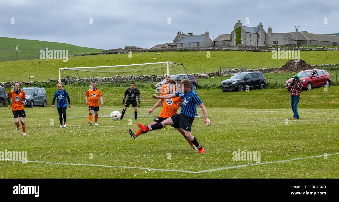 Pierowall, Westray, Orcades, Écosse, Royaume-Uni. Papa Westray v Sanday 2nd leg football matc in Orkney amateur Football Association League ou Orcadian Cup : la famille Houston trigénérationnelle) dans l'équipe de Papa Westray (alias les Doondies en maillots orange) allant dans l'âge de 63 à 19 ans, avec une population de 90 et aucun terrain de football à pratiquer sur perdre 7-1 ayant perdu 6-0 dans la 1ère manche. Ils étaient ravis de marquer un but avec un penalty dans les dernières minutes du match. De nombreux habitants de Papa Westray sont venus de l'île pour les soutenir. Crédit : Sally Anderson/Alamy Live News Banque D'Images