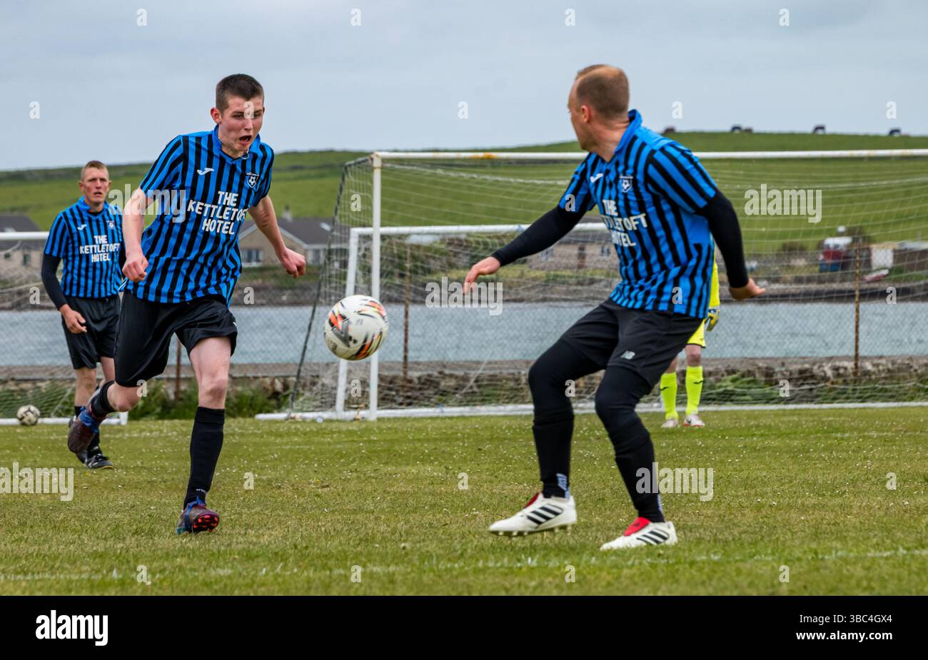 Pierowall, Westray, Orcades, Écosse, Royaume-Uni. Papa Westray v Sanday 2nd leg football matc in Orkney amateur Football Association League ou Orcadian Cup : la famille Houston trigénérationnelle) dans l'équipe de Papa Westray (alias les Doondies en maillots orange) allant dans l'âge de 63 à 19 ans, avec une population de 90 et aucun terrain de football à pratiquer sur perdre 7-1 ayant perdu 6-0 dans la 1ère manche. Ils étaient ravis de marquer un but avec un penalty dans les dernières minutes du match. De nombreux habitants de Papa Westray sont venus de l'île pour les soutenir. Crédit : Sally Anderson/Alamy Live News Banque D'Images