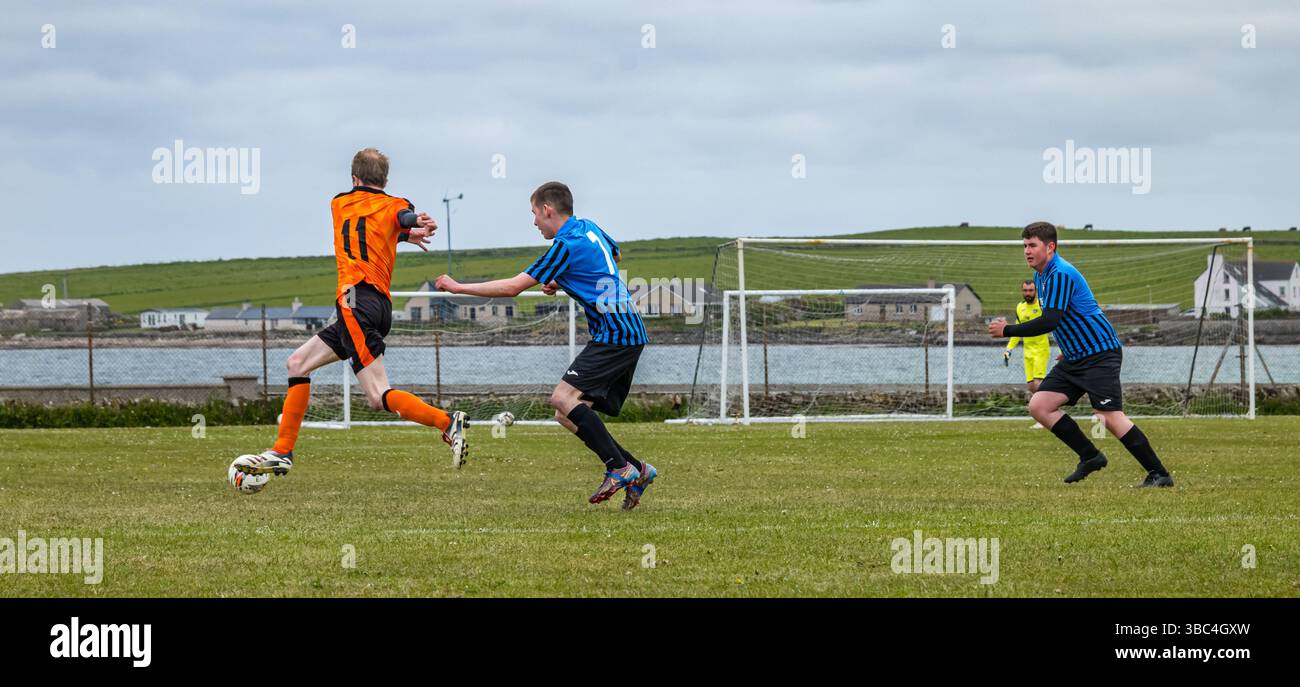 Pierowall, Westray, Orcades, Écosse, Royaume-Uni. Papa Westray v Sanday 2nd leg football matc in Orkney amateur Football Association League ou Orcadian Cup : la famille Houston trigénérationnelle) dans l'équipe de Papa Westray (alias les Doondies en maillots orange) allant dans l'âge de 63 à 19 ans, avec une population de 90 et aucun terrain de football à pratiquer sur perdre 7-1 ayant perdu 6-0 dans la 1ère manche. Ils étaient ravis de marquer un but avec un penalty dans les dernières minutes du match. De nombreux habitants de Papa Westray sont venus de l'île pour les soutenir. Crédit : Sally Anderson/Alamy Live News Banque D'Images