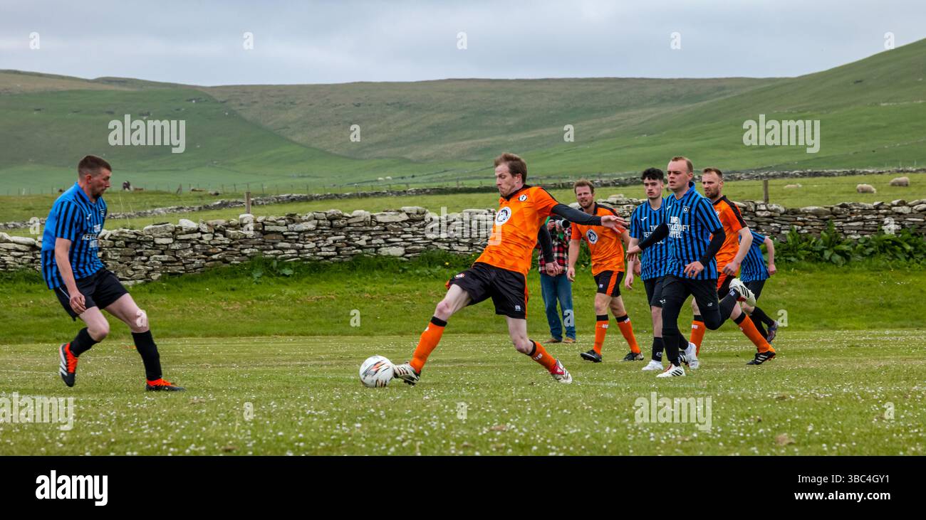 Pierowall, Westray, Orcades, Écosse, Royaume-Uni. Papa Westray v Sanday 2nd leg football matc in Orkney amateur Football Association League ou Orcadian Cup : la famille Houston trigénérationnelle) dans l'équipe de Papa Westray (alias les Doondies en maillots orange) allant dans l'âge de 63 à 19 ans, avec une population de 90 et aucun terrain de football à pratiquer sur perdre 7-1 ayant perdu 6-0 dans la 1ère manche. Ils étaient ravis de marquer un but avec un penalty dans les dernières minutes du match. De nombreux habitants de Papa Westray sont venus de l'île pour les soutenir. Crédit : Sally Anderson/Alamy Live News Banque D'Images