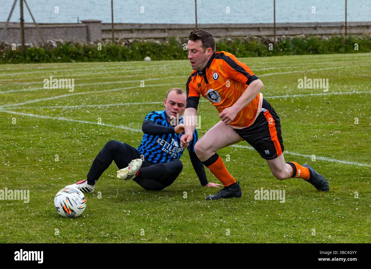 Pierowall, Westray, Orcades, Écosse, Royaume-Uni. Papa Westray v Sanday 2nd leg football matc in Orkney amateur Football Association League ou Orcadian Cup : la famille Houston trigénérationnelle) dans l'équipe de Papa Westray (alias les Doondies en maillots orange) allant dans l'âge de 63 à 19 ans, avec une population de 90 et aucun terrain de football à pratiquer sur perdre 7-1 ayant perdu 6-0 dans la 1ère manche. Ils étaient ravis de marquer un but avec un penalty dans les dernières minutes du match. De nombreux habitants de Papa Westray sont venus de l'île pour les soutenir. Crédit : Sally Anderson/Alamy Live News Banque D'Images