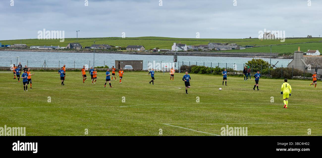 Pierowall, Westray, Orcades, Écosse, Royaume-Uni. Papa Westray v Sanday 2nd leg football matc in Orkney amateur Football Association League ou Orcadian Cup : la famille Houston trigénérationnelle) dans l'équipe de Papa Westray (alias les Doondies en maillots orange) allant dans l'âge de 63 à 19 ans, avec une population de 90 et aucun terrain de football à pratiquer sur perdre 7-1 ayant perdu 6-0 dans la 1ère manche. Ils étaient ravis de marquer un but avec un penalty dans les dernières minutes du match. De nombreux habitants de Papa Westray sont venus de l'île pour les soutenir. Crédit : Sally Anderson/Alamy Live News Banque D'Images