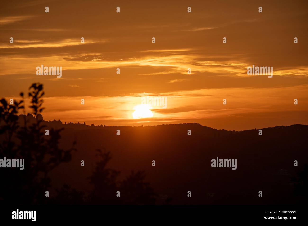 Coucher de soleil éclatant derrière une chaîne de montagnes silhouette, peignant le ciel dans des tons dorés. Banque D'Images