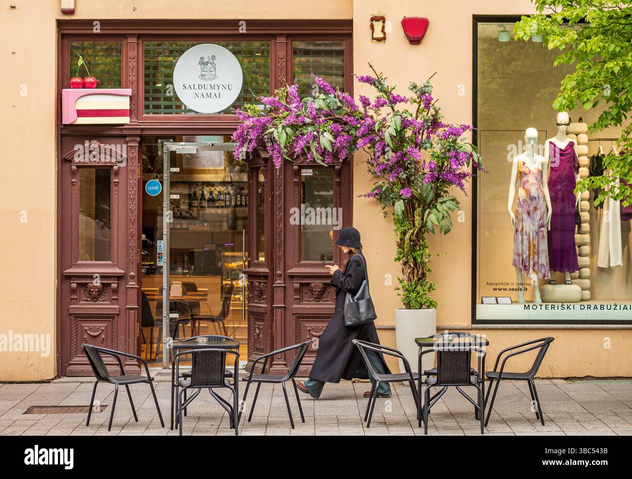 La jeune fille se promène en regardant son smartphone dans les rues du centre de Vilnius, devant un café avec des tables à l'extérieur Banque D'Images