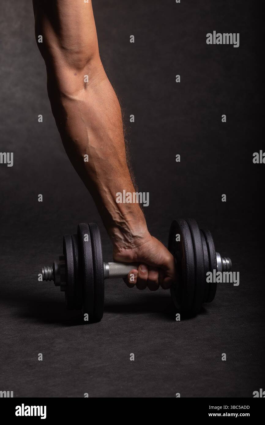haltère à une main pour l'haltérophilie tenu par une main masculine forte et bien entraînée sur un fond noir Banque D'Images