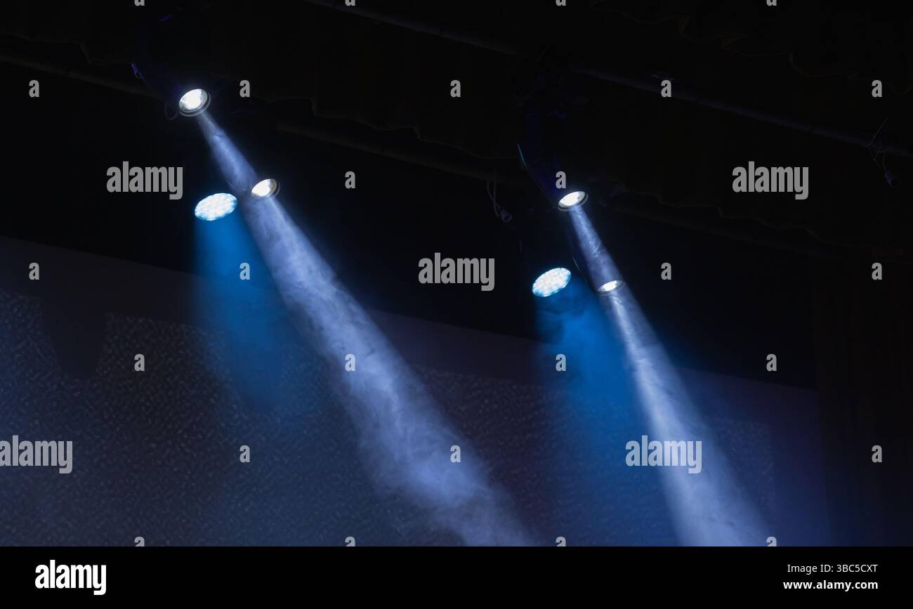 Les projecteurs brillent de manière éclatante, produisant des faisceaux de lumière visibles dans un environnement de scène faiblement éclairé, évoquant un sentiment de drame et de concentration, idéal pour la performance Banque D'Images