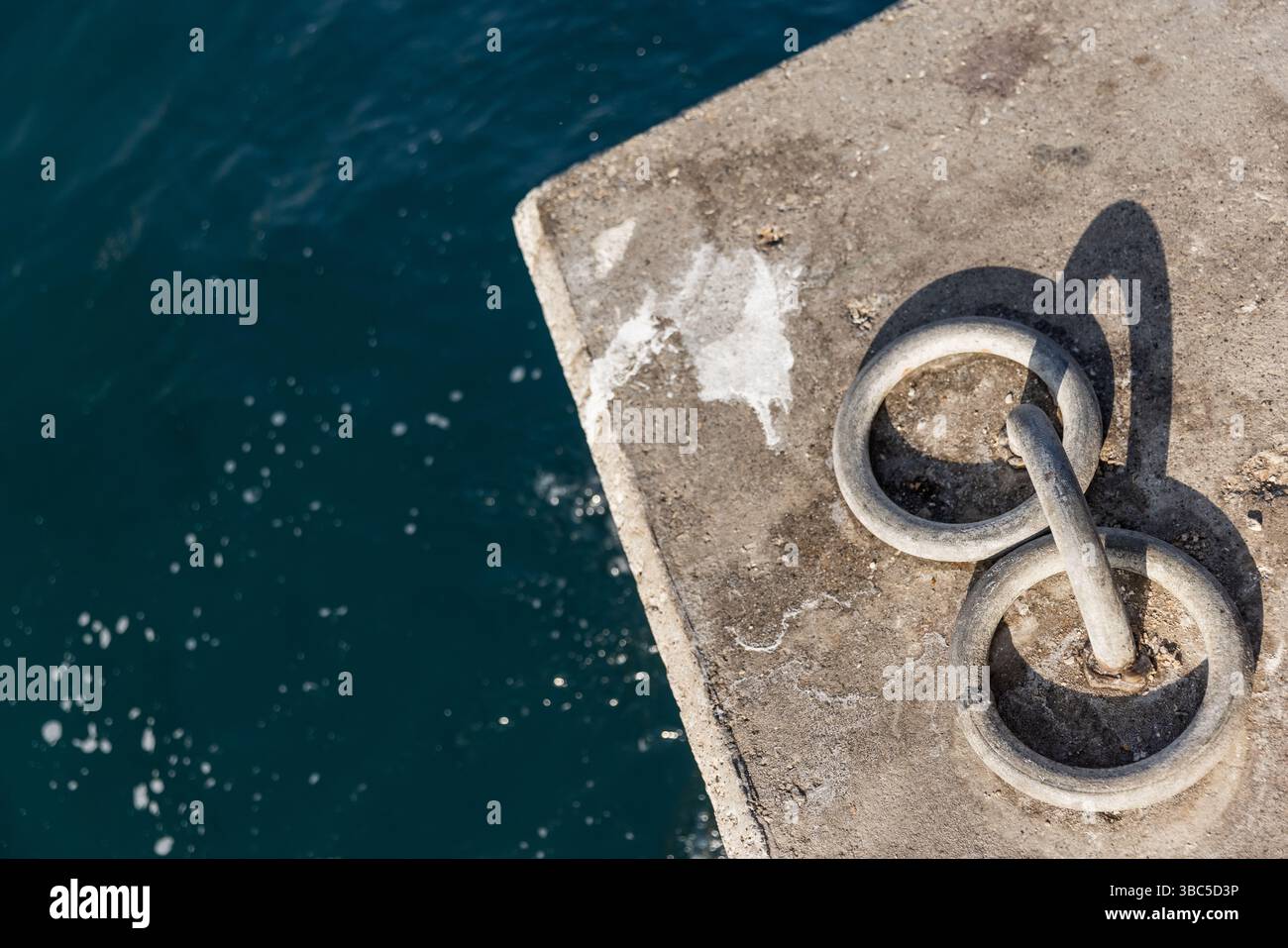 Anneaux d'amarrage métalliques encastrés dans une surface de béton au bord de l'eau bleu profond Banque D'Images