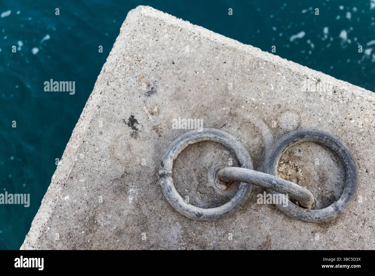 Une vue détaillée de deux anneaux d'amarrage interconnectés encastrés dans une surface de béton près d'une eau bleue calme Banque D'Images