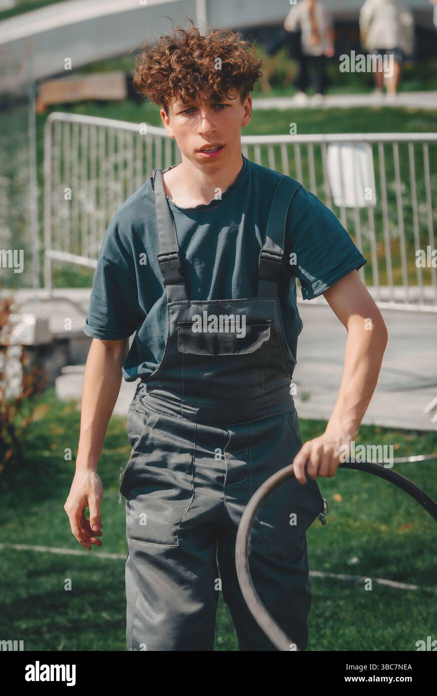 jeune jardinier avec un tuyau dans la main marche sur l'herbe Banque D'Images