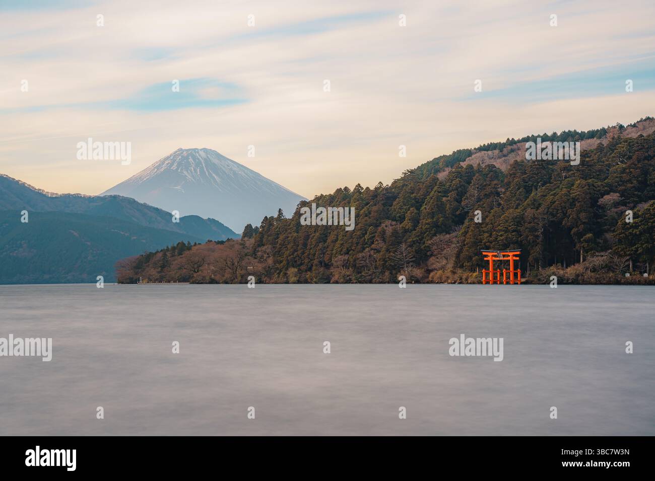 Vue panoramique d'une porte torii rouge traditionnelle debout dans le lac Ashi avec des collines boisées en arrière-plan. Banque D'Images