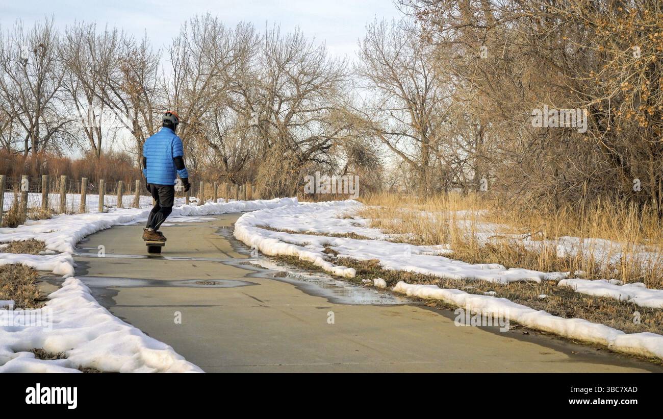 Un pilote masculin se déplace sur une planche à roulettes électrique le long d'une piste cyclable dans un paysage hivernal dans le nord du Colorado - Colorado Front Range Trail dans l'État de Boyd Lake Banque D'Images