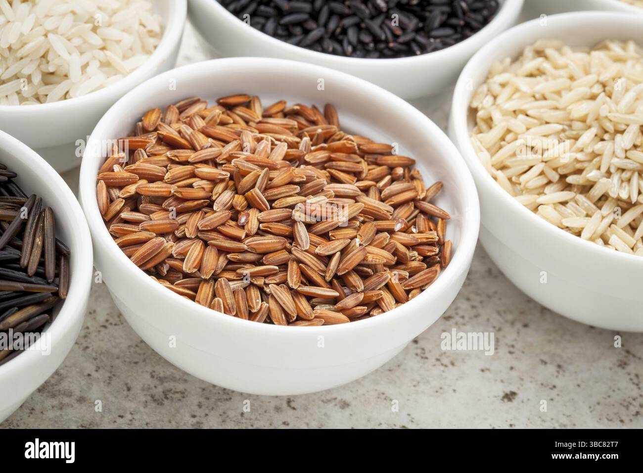 Un petit bol de grain de riz brun parmi des bols d'autres grains Banque D'Images