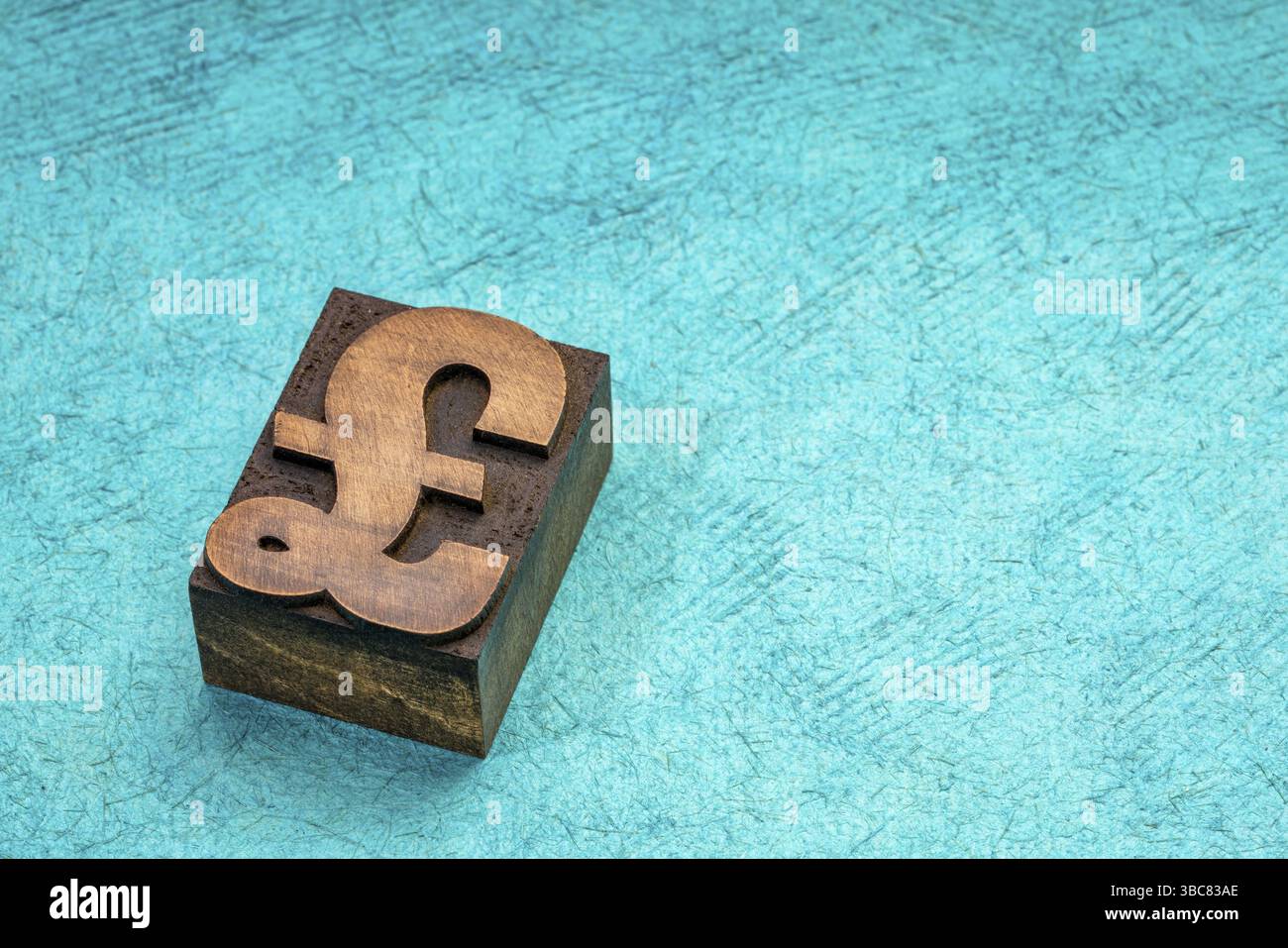 La livre sterling du symbole dans la typographie type de bloc d'impression turquoise contre du papier fait à la main avec une copy space Banque D'Images