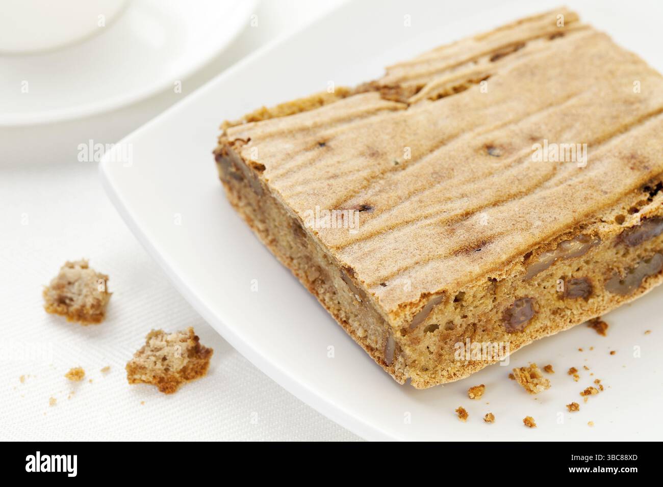 Un morceau et des miettes de pain sans gluten fait maison à base de farines de noix de coco, de millet et de riz brun, de riz et de son, de wlanuts et de raisins secs - plaque blanche A. Banque D'Images