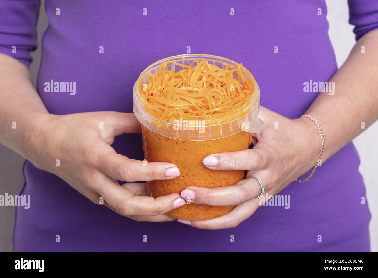 Mains tenant un seau en plastique de carottes marinées Banque D'Images