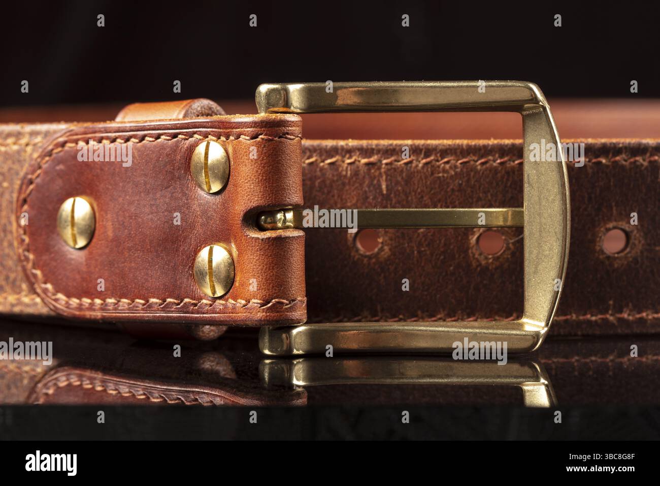 Partie d'une ceinture en cuir marron avec une boucle en métal sur fond noir Banque D'Images