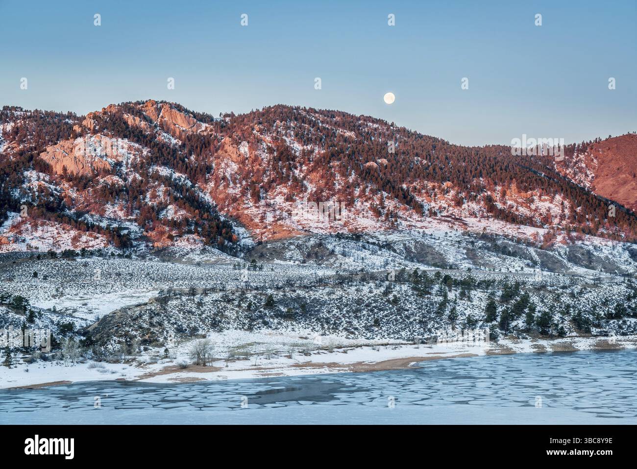 Lune se couche sur Arhturs Rock allumé par sunrise avec réservoir Horsetooth couverte de glace, Fort Collins, Colorado Banque D'Images