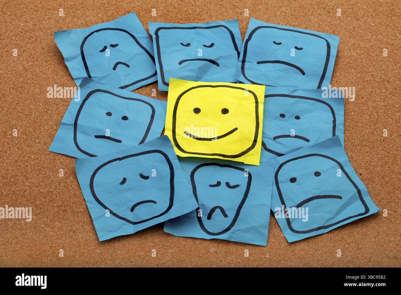Attitude positive ou concept d'optimisme - visage souriant heureux sur note collante jaune entouré de visages bleus tristes malheureux Banque D'Images