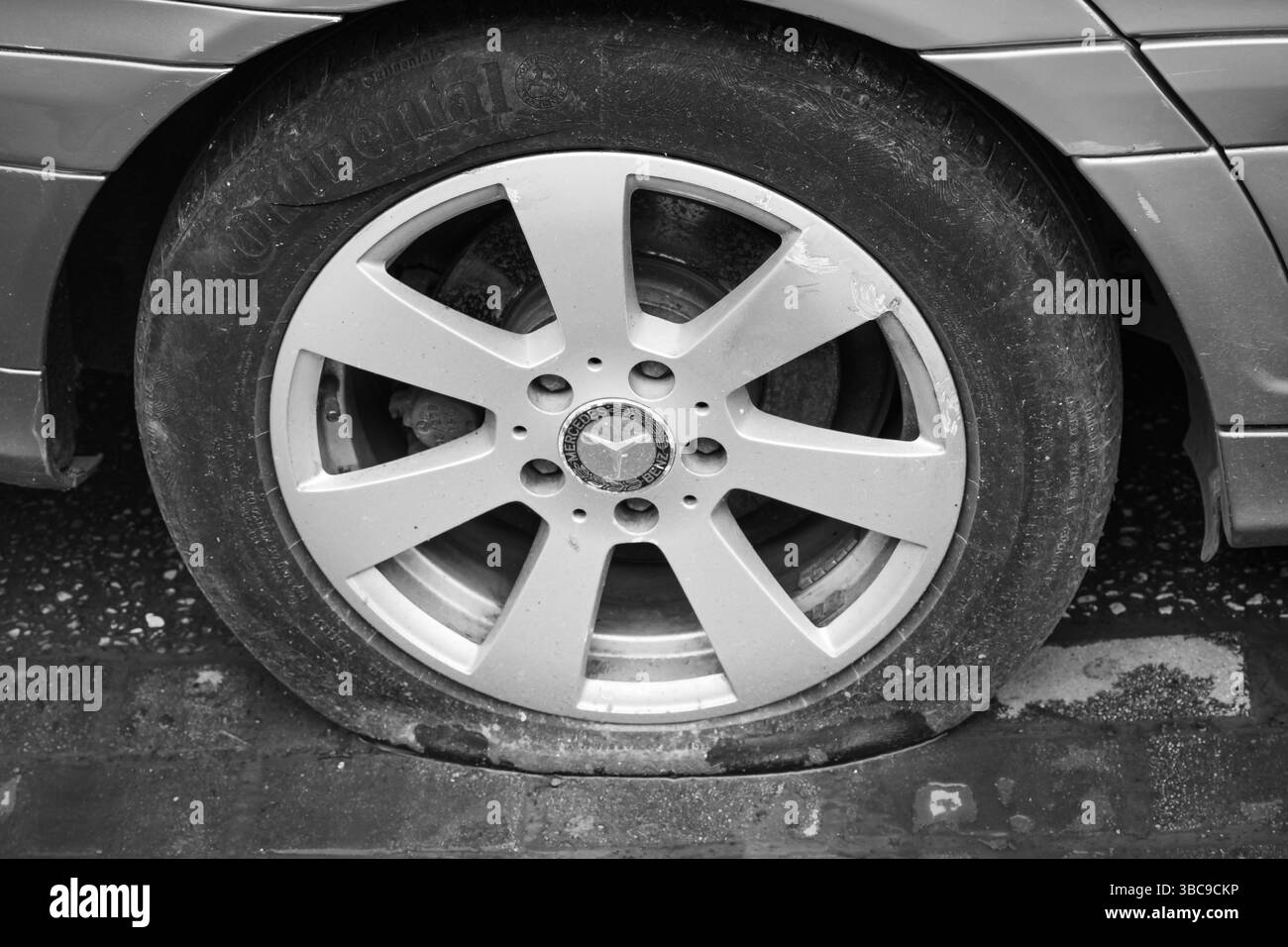 Gros plan pneu de voiture à plat, perte de pression des pneus sur une route. Pneu arrière plat sur une voiture Mercedes Benz, crevaison de pneu. Véhicule avec caoutchouc perforé sur un wh Banque D'Images