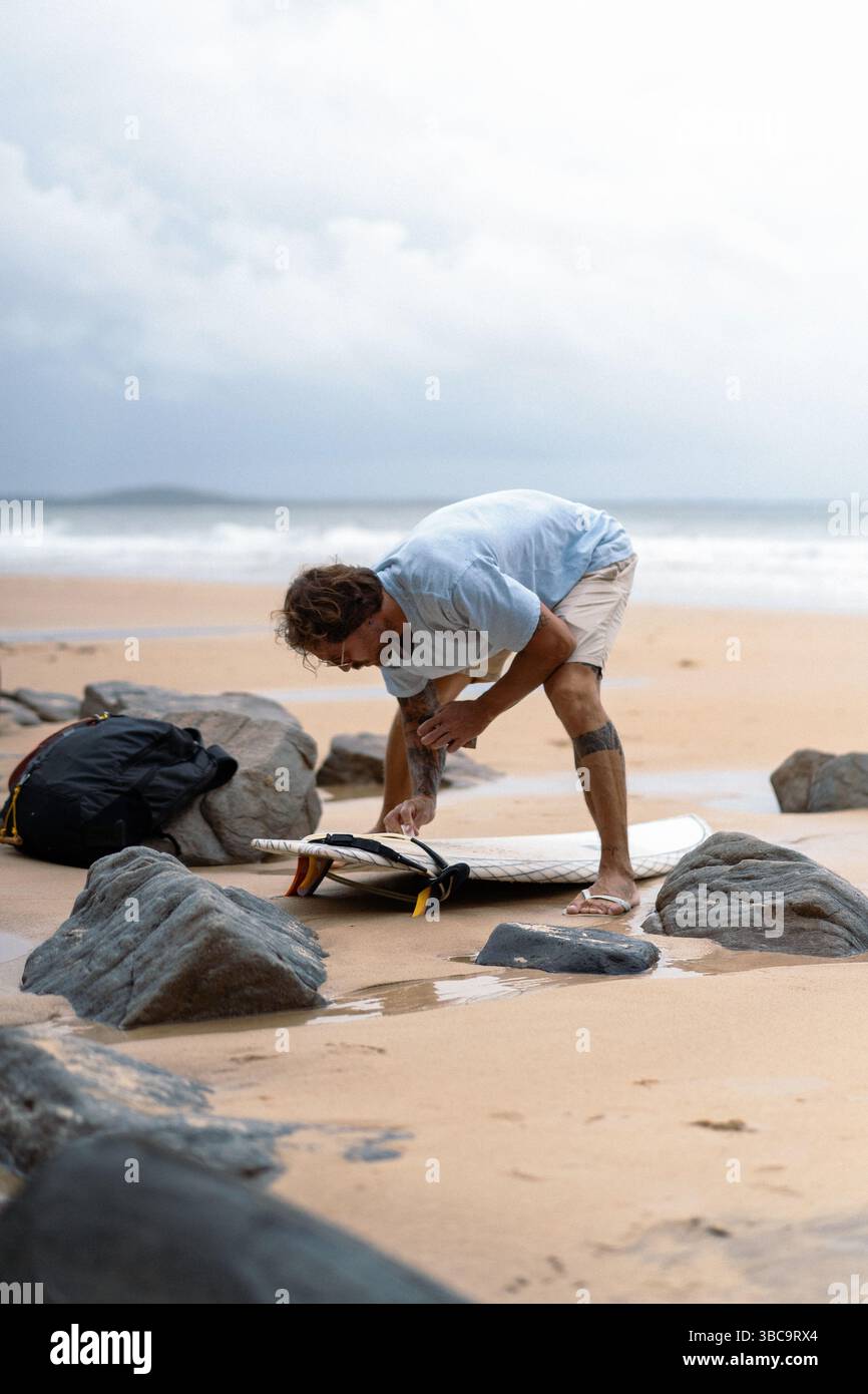 L'homme cire sa planche sur la plage avant de surfer Banque D'Images