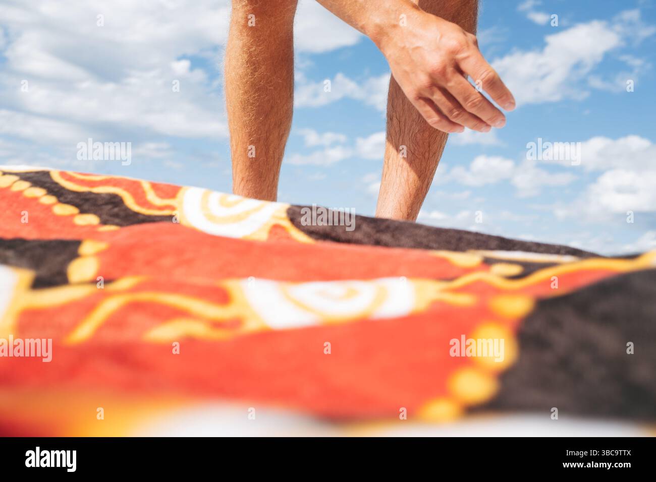 Homme atteignant au-dessus d'une serviette de plage à motifs sous un ciel bleu vif Banque D'Images