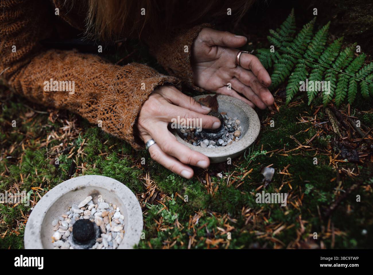 Mains allumant une boule d'encens faite à la main dans un cadre rituel de forêt. Banque D'Images