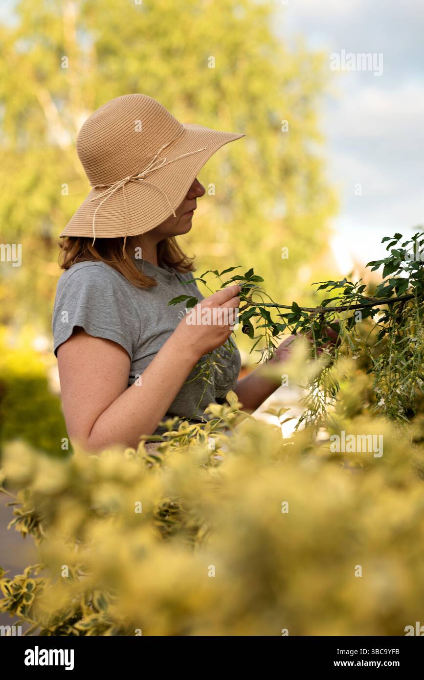 Femme dans un chapeau de paille touchant une branche d'arbre dans le jardin. Banque D'Images