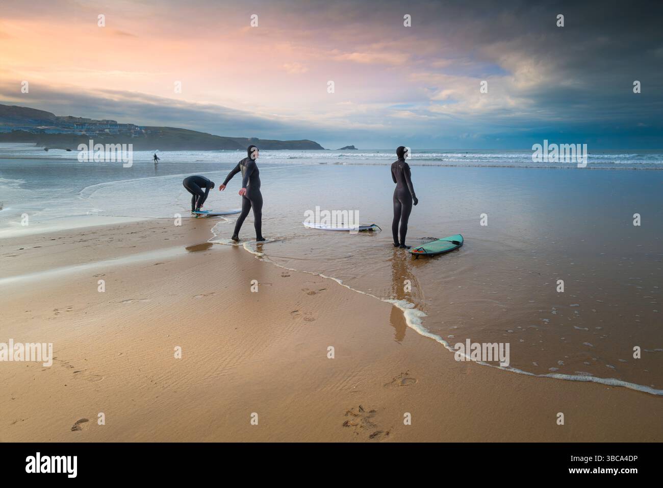 Un groupe de trois surfeurs debout et se préparant pour une séance de surf sur Fistral Beach à Newquay en Cornouailles au Royaume-Uni. Banque D'Images