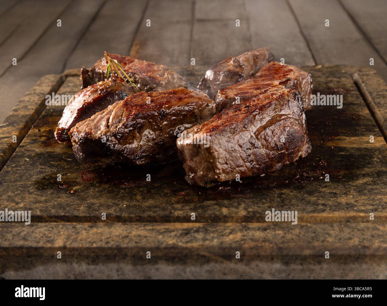 Tranches de steak grillé garnies d'herbes fraîches sur une surface en pierre Banque D'Images