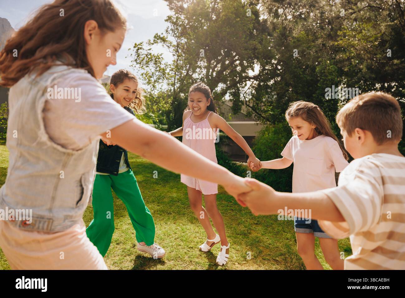 Un groupe d'enfants se tenant la main et jouant ensemble dans un parc ensoleillé, favorisant l'amitié et le plaisir en plein air. Banque D'Images