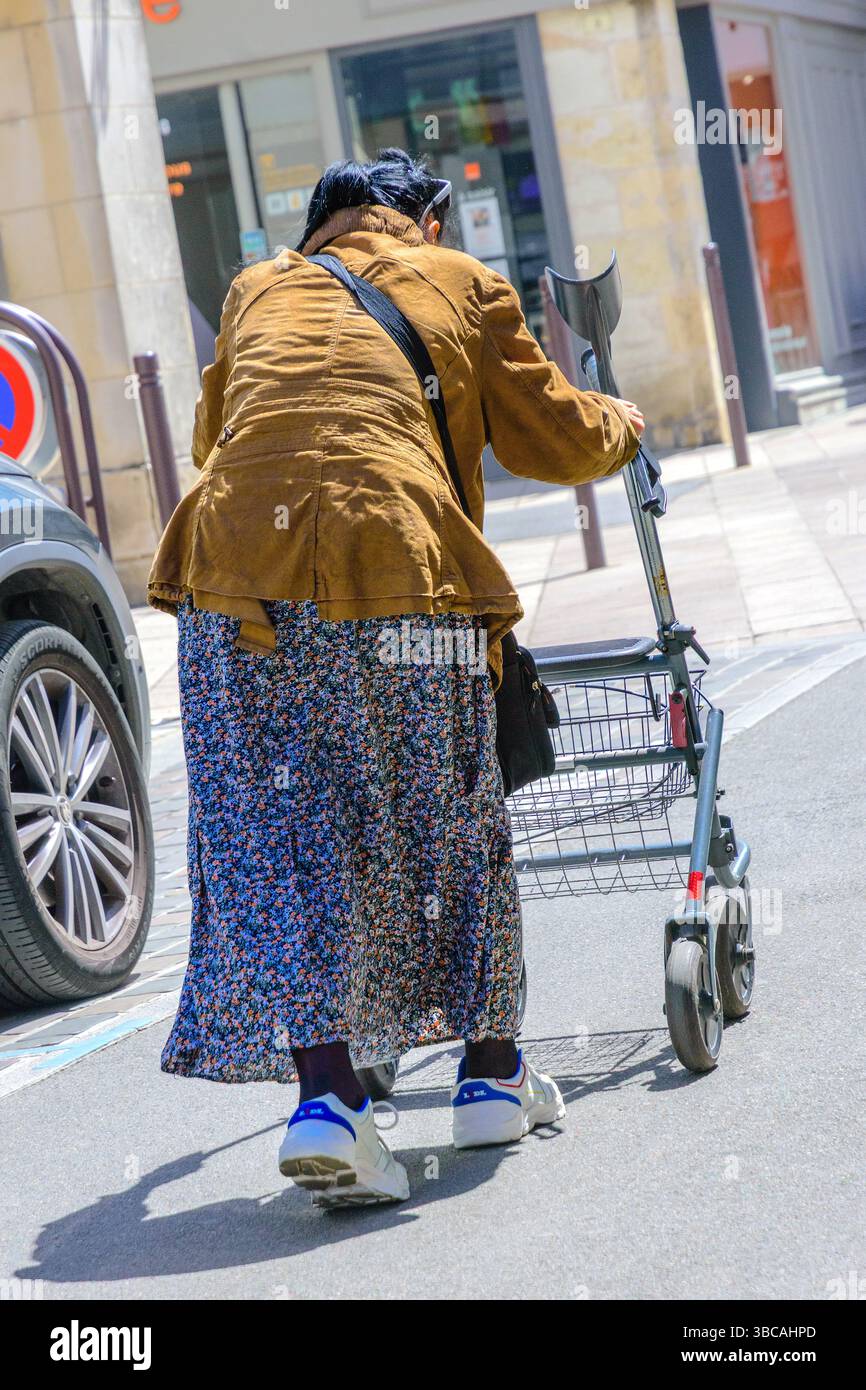 Vue arrière d'une femme âgée penchée vers l'avant avec cadre de marche à roues - Loches, Indre-et-Loire (37), France. Banque D'Images