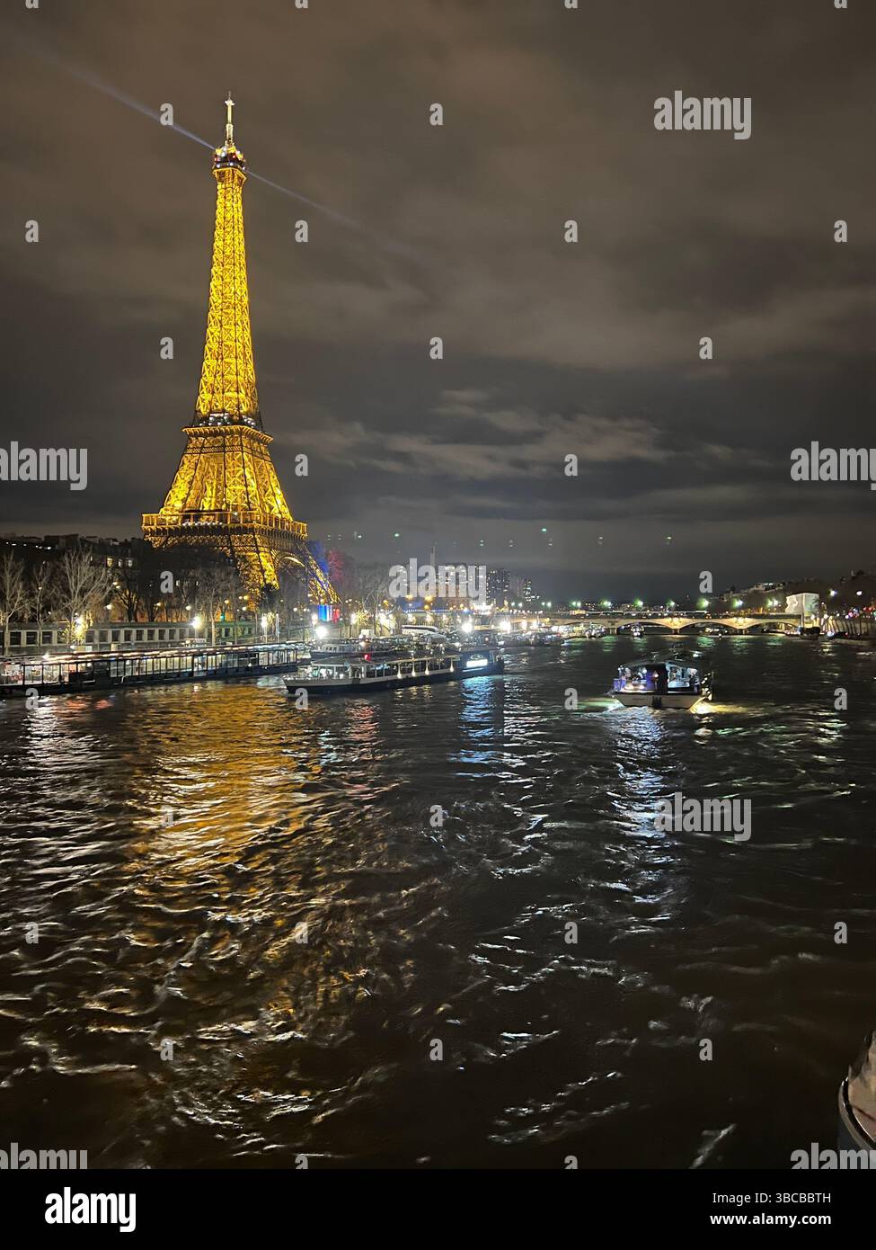 La Tour Eiffel brille au-dessus de la Seine à Paris, en France, projetant des reflets chatoyants sur l'eau lors d'une excursion nocturne en bateau. Banque D'Images